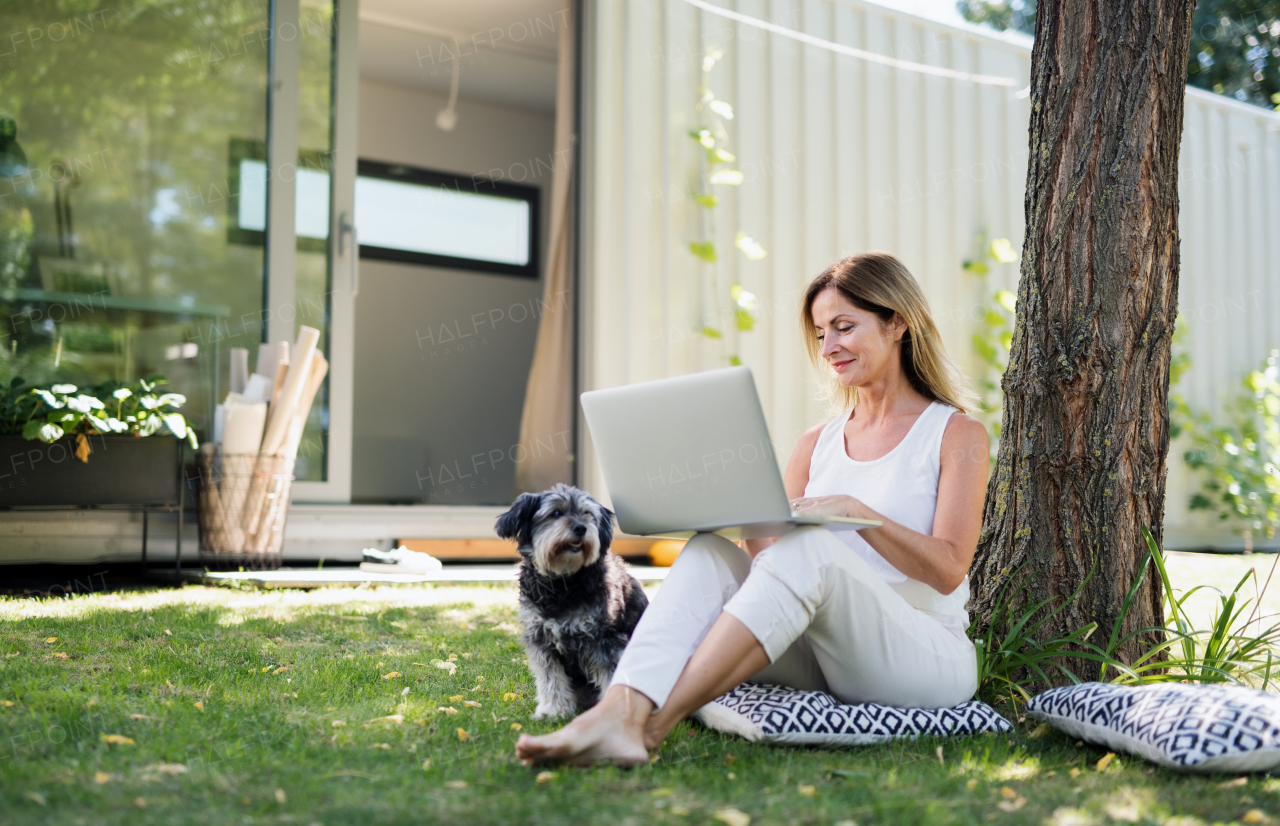 Mature woman with pet dog working in home office outdoors in garden, using laptop.