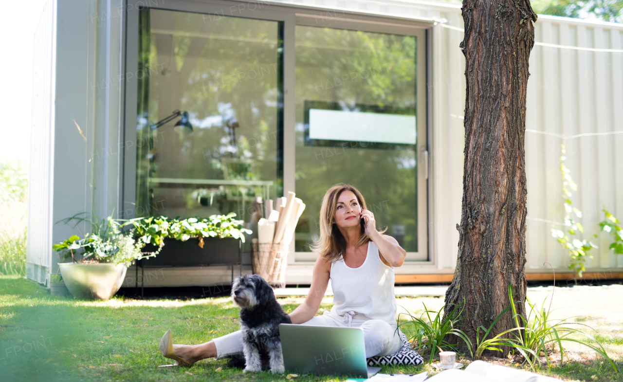 Mature woman with pet dog working in home office outdoors in garden, using laptop.