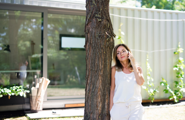 Mature woman with pet dog working in home office outdoors in garden, using smartphone.