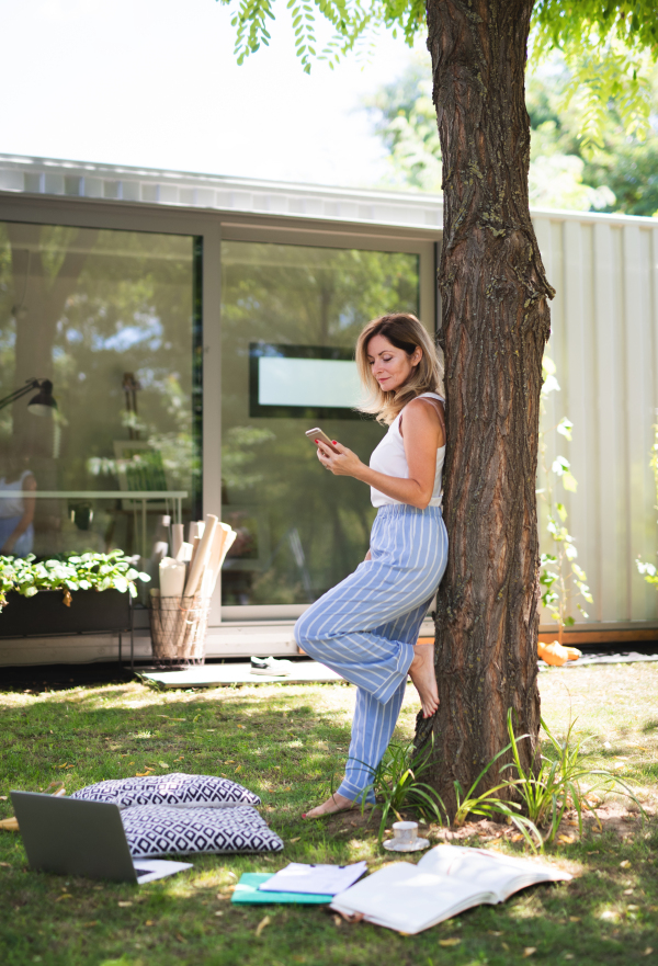 Happy mature woman working in home office outdoors in garden, using smartphone.