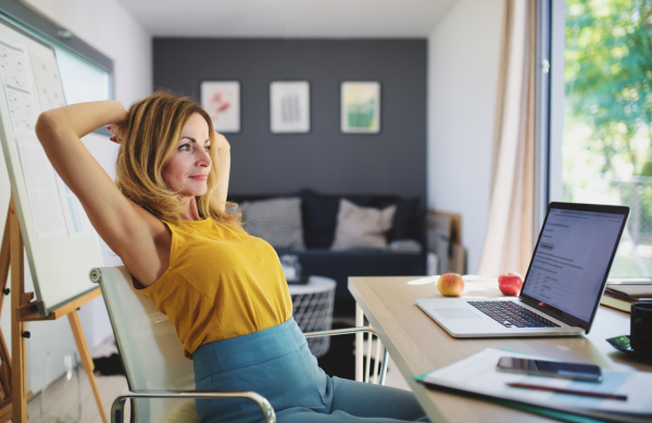 Side view of mature woman working indoors in home office in container house in backyard, resting.