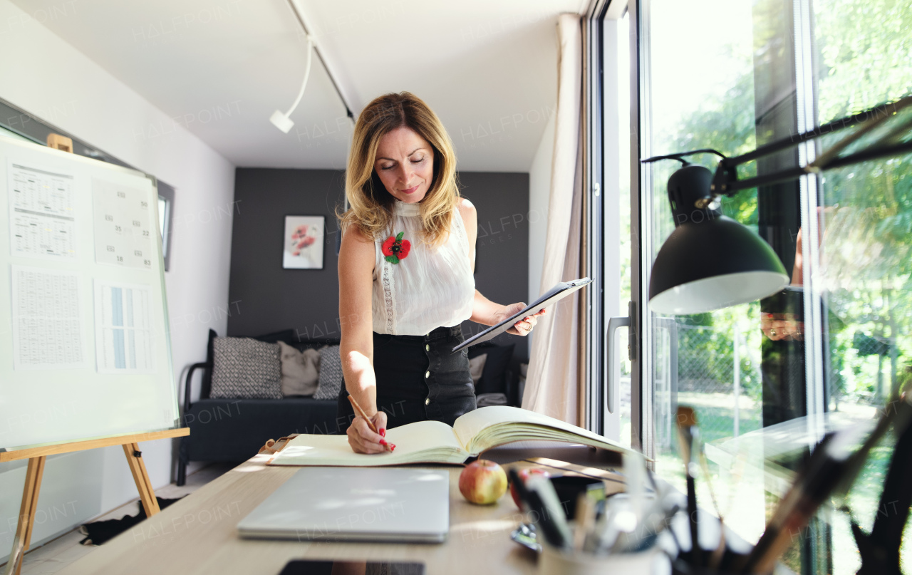 Front view of mature woman working indoors in home office in container house in backyard.