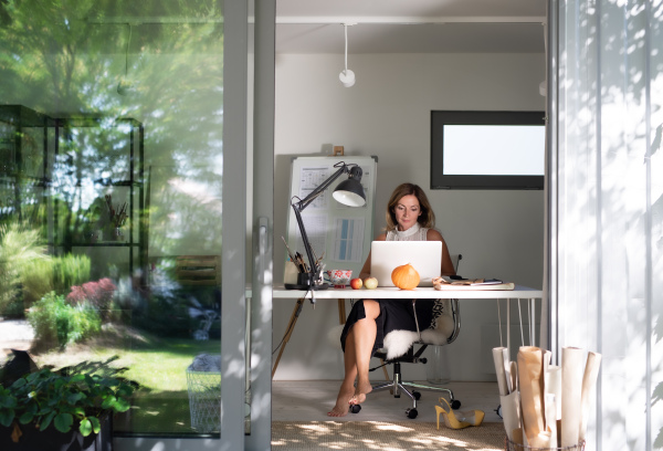 Front view of mature woman working indoors in home office in container house in backyard.