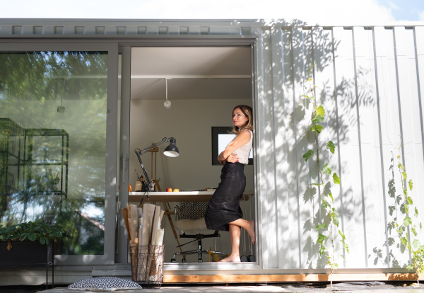 Side view of mature woman working in home office in container house in backyard, resting.