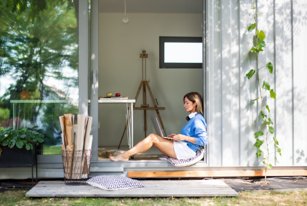 Happy mature woman working in home office in container house in backyard.