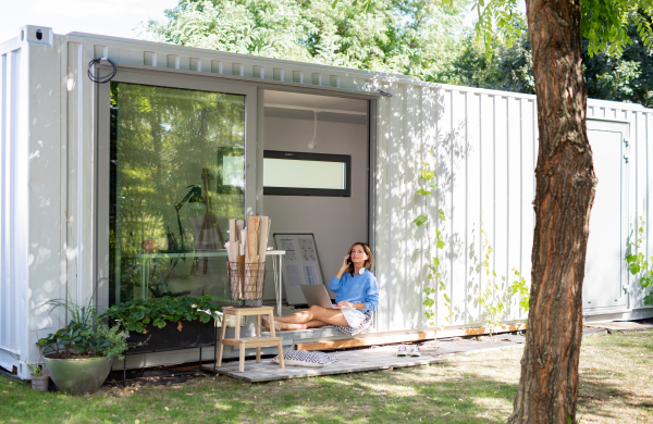 Happy mature woman working in home office in container house in backyard.