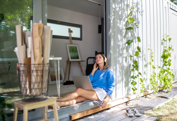 Front view of mature woman working in home office in container house in backyard.