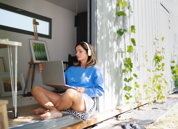 Front view of mature woman working in home office in container house in backyard.