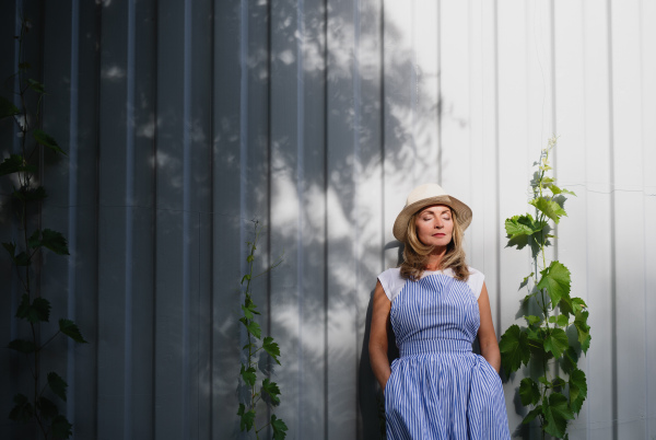 Portrait of mature woman standing outdoors in garden, relaxing with eyes closed. Copy space.