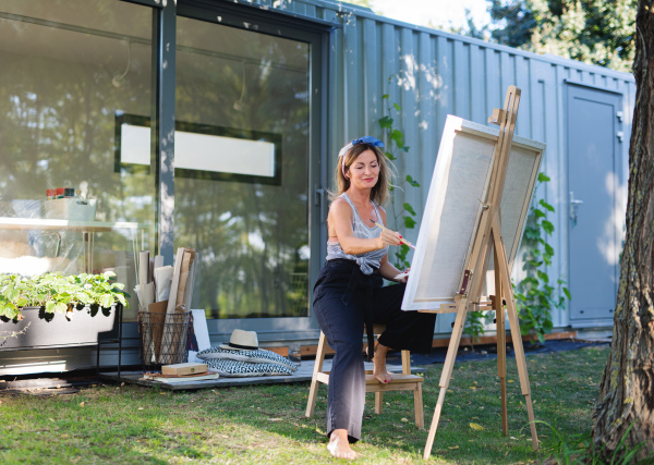 Portrait of happy mature woman with pallete painting outdoors in garden.