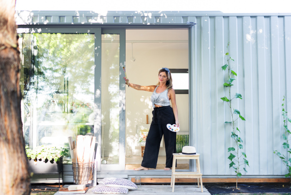 Portrait of happy mature woman with pallete painting in container house.