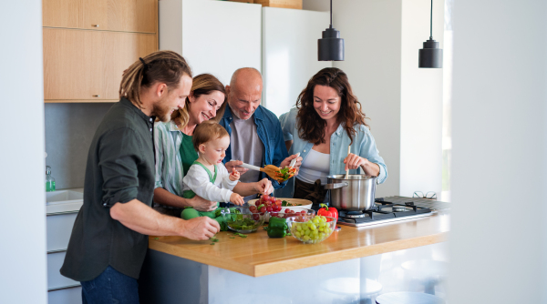 Happy multigeneration family indoors at home preparing vegetable salad in kitchen.