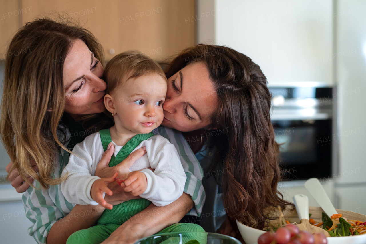 Portrait of happy mother and grandmother kissing small baby indoors at home.