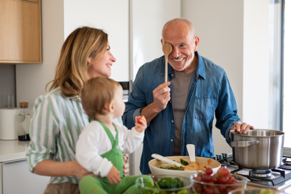 Happy senior couple with granddaughter indoors at home, cooking.