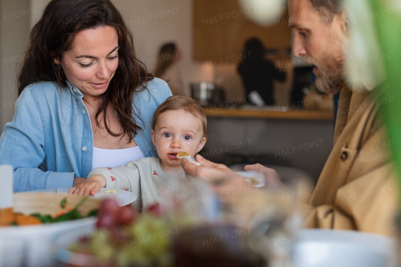 Portrait of happy couple indoors at home eating lunch at the table, feeding baby.