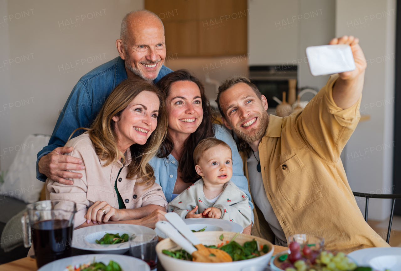 Happy multigeneration family indoors at home eating healthy lunch, taking selfie with smartphone.