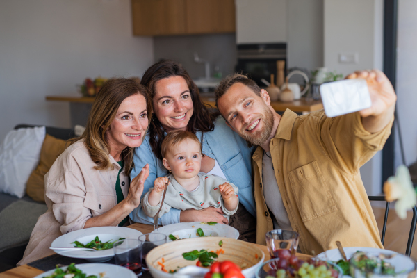 Happy multigeneration family indoors at home eating healthy lunch, taking selfie with smartphone.