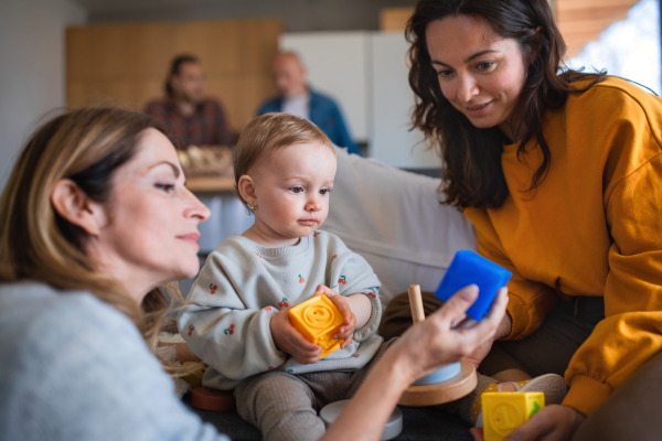 A happy multigeneration family playing with small baby indoors at home, visiting concept.