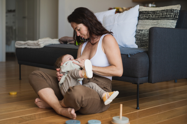 Happy young mother nursing small baby indoors at home, breastfeeding concept.