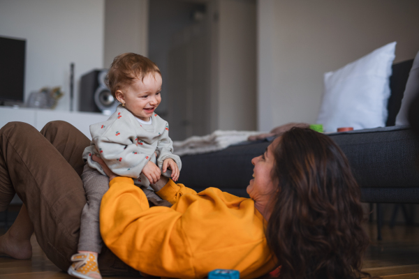 Portrait of young mother playing with small baby indoors at home, having fun.