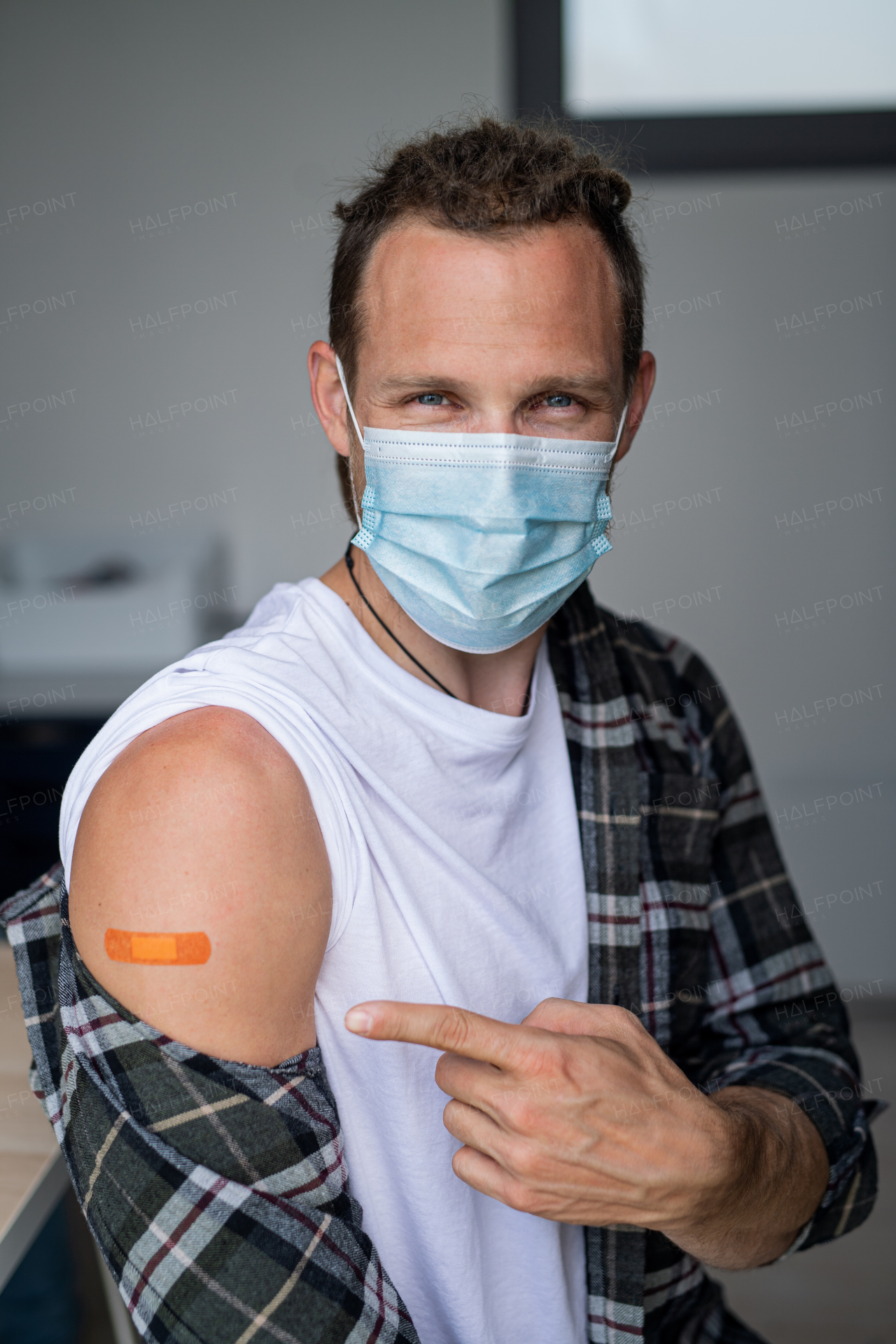 Portrait of happy mid adult man after covid-9 vaccination, pointing to plaster on arm and looking at camera.