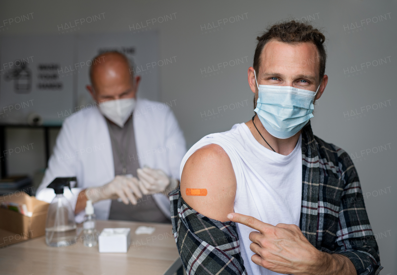 Portrait of happy mid adult man after covid-9 vaccination, pointing to plaster on arm and looking at camera.