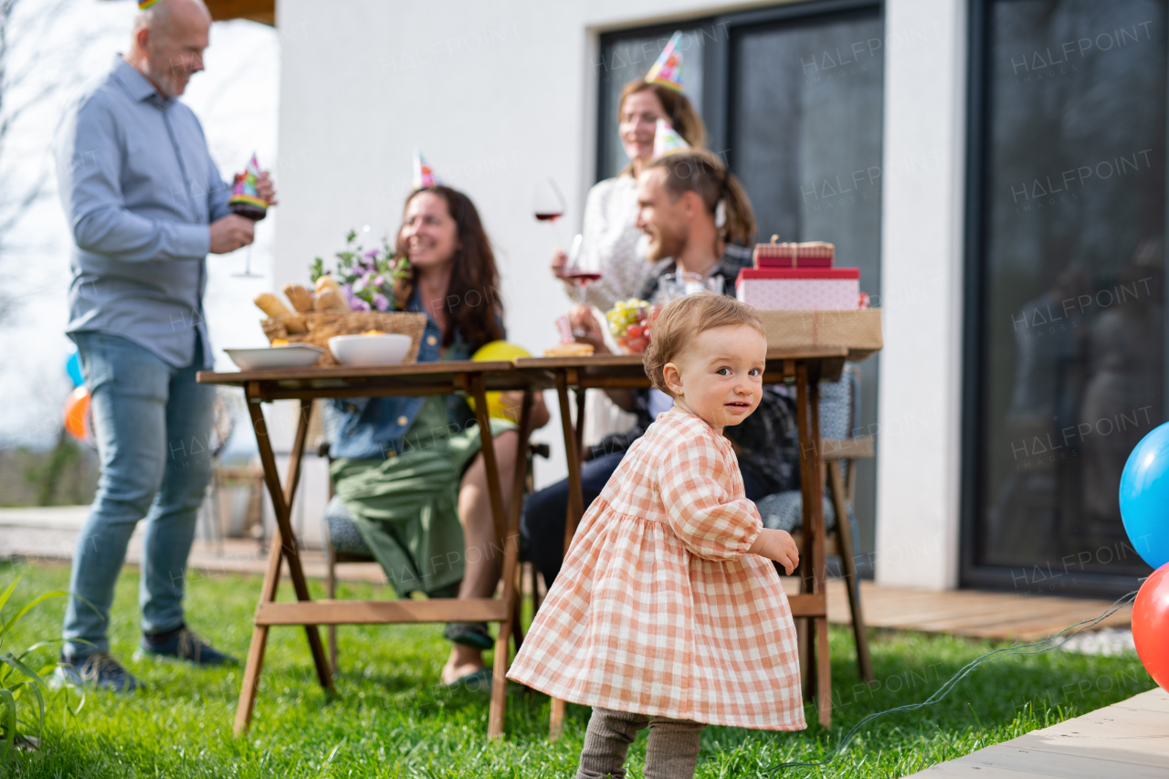 A small toddler with parents and grandparents outdoors in garden at home, birthday celebration party.