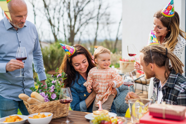 A happy multigeneration family outdoors in garden at home, birthday celebration party.