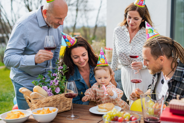 A happy multigeneration family outdoors in garden at home, birthday celebration party.