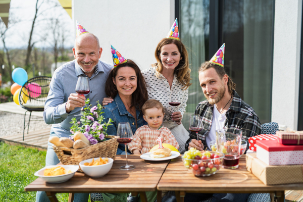 A happy multigeneration family outdoors in garden at home, birthday celebration party.