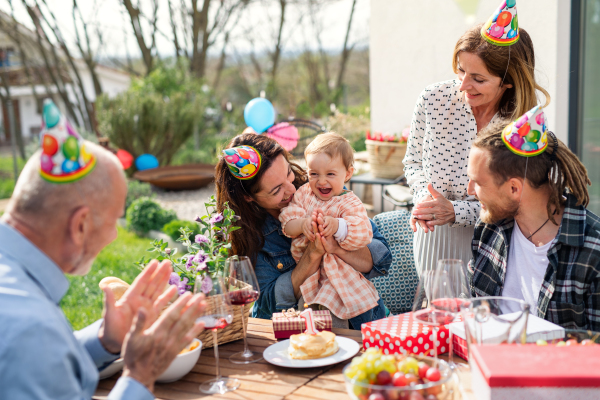 A happy multigeneration family outdoors in garden at home, birthday celebration party.