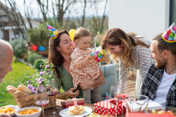 A happy multigeneration family outdoors in garden at home, birthday celebration party.