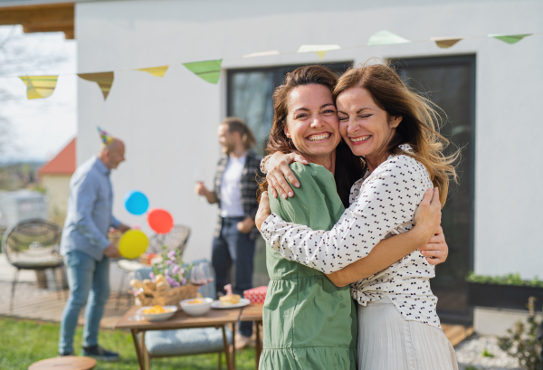 Portrait of young woman with mother outdoors in garden at home, birthday celebration party.