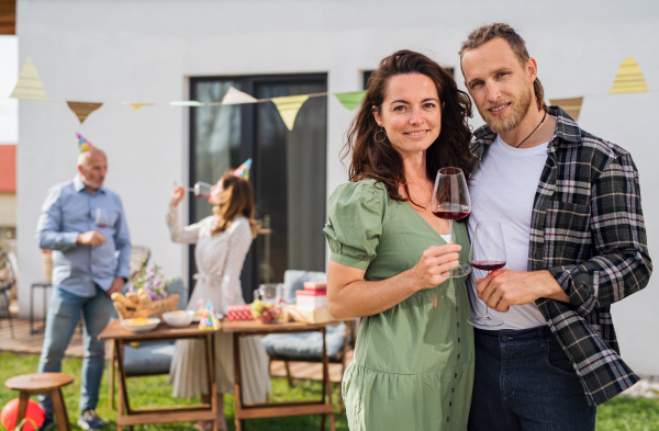 A young couple with wine outdoors in garden at home, birthday celebration party.