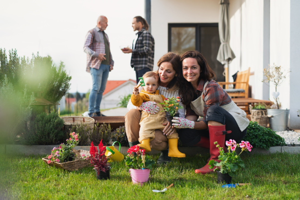 A happy multigeneration family outdoors planting flowers in garden at home, gardening concept.