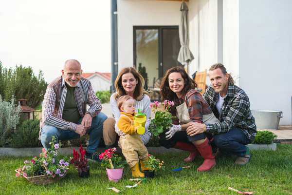 A happy multigeneration family outdoors planting flowers in garden at home, gardening concept.