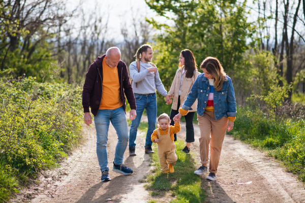 Small toddler with parents and grandparents on a walk outdoors in nature, looking at camera.