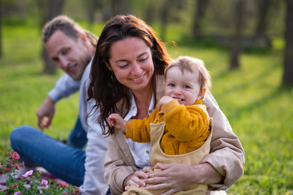 Portrait of happy young parents with small baby daughter sitting on grass in nature, relaxing.