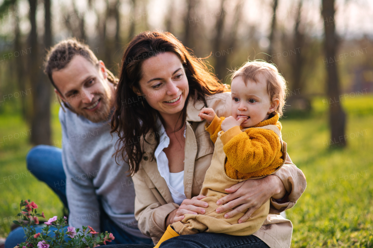 Portrait of happy young parents with small baby daughter sitting on grass in nature, relaxing.