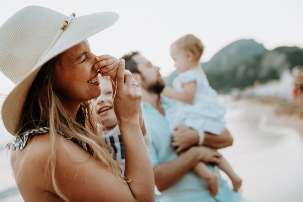 A young family with two toddler children standing on beach on summer holiday, having fun.