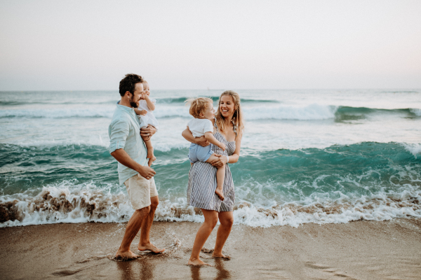 A young family with two toddler children walking on beach on summer holiday.