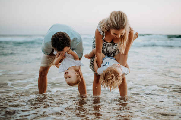 A young family with two toddler children standing on beach on summer holiday, having fun.