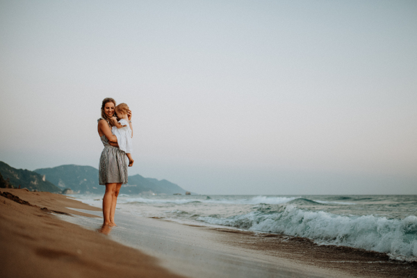 A young mother with a toddler girl on beach on summer holiday. Copy space.