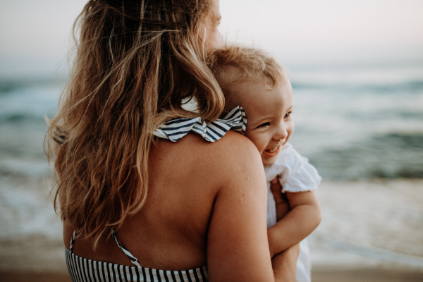 A close-up of young mother with a toddler girl on beach on summer holiday.