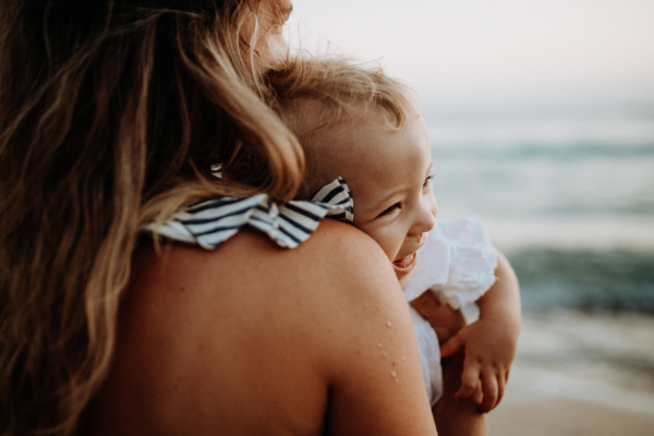 A close-up of young mother with a toddler girl on beach on summer holiday.