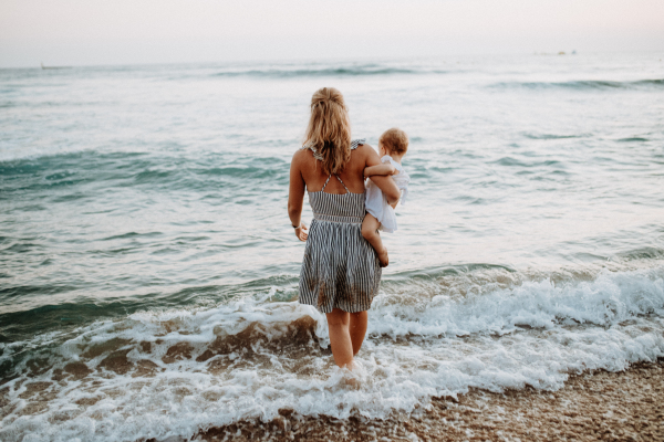 A rear view of young mother with a toddler girl walking in sea on summer holiday.