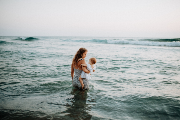 A rear view of young mother with a toddler girl walking in sea on summer holiday.