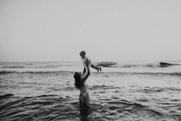 A young mother with a toddler girl on beach on summer holiday, having fun.