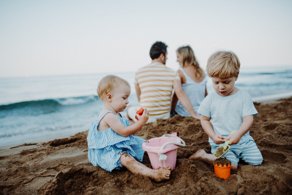 Toddler children with parents playing on sand beach on summer family holiday.