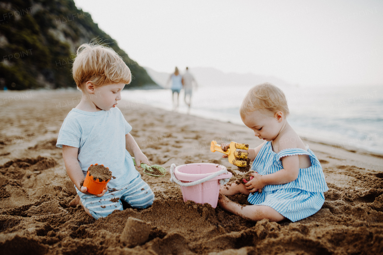 Two toddler children playing on sand beach on summer family holiday.